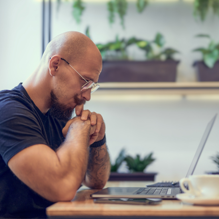 Frustrated man sitting at home office desk looking down at his laptop, facing freelance writing challenges.